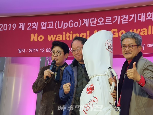 '2019 제2회 업고(UpGo)계단오르기걷기대회 및 불우이웃돕기 문화공연' 후원업체 1879그룹 이동현 회장(좌측)이 자사제품 골프백을 경품 당첨자에게 전달하고 있다.