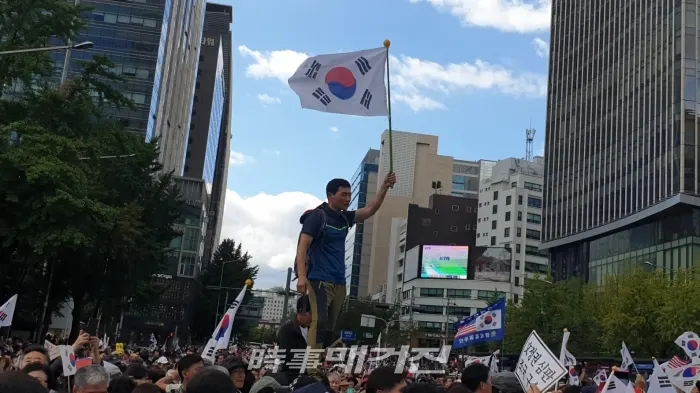 태극기를 들고 높은곳에 올라 연설을 경청하는 젊은 참가자